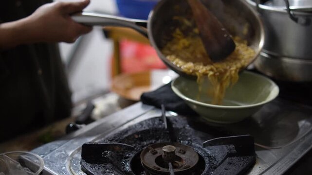 Anonymous woman cooking instant noodles or "Mie Nyemek" in a pan, stirring noodles with savory thick sauce and spices in a home kitchen