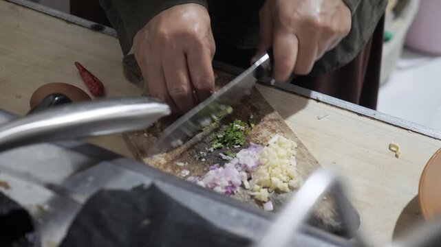 Close up of anonymous woman hands chopping and slicing fresh green celery or coriander leaves on a wooden cutting board