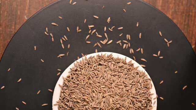 Top View of Cumin Seeds (Jeera) in White Bowl on Black Background &ndash; Rotating Footage