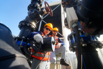Two engineers in hard hats and safety vests working on industrial pipes and valves outdoors