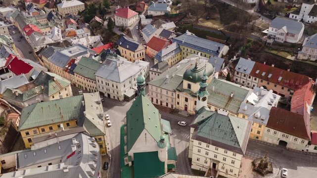 Top down aerial drone shot of Holy Trinity Square in Banska Stiavnica, Slovakia. Historic church, baroque architecture and colorful rooftops in UNESCO old town center.