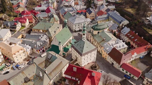 Dynamic aerial drone view of Banska Stiavnica old town in Slovakia. Historic square, church towers and colorful rooftops in UNESCO heritage mining city.