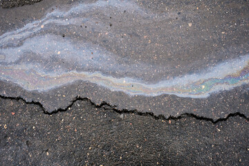 Oil slick on wet asphalt pavement with iridescent colors, forming a rainbow pattern, symbolizing pollution and environmental impact