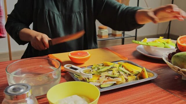 Woman slicing fresh grapefruit on yellow cutting board for healthy fruit salad