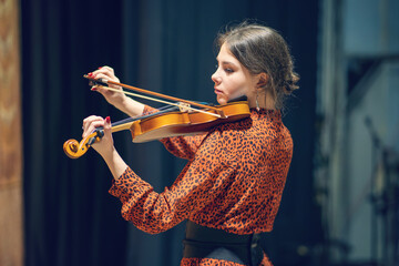 young, beautiful woman in a brown dress plays the violin on stage. © diy13