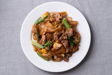 Thai food (Pad See Ew), Stir-fried rice noodles with soy sauce, pork, egg, and kale on a white plate, Top view