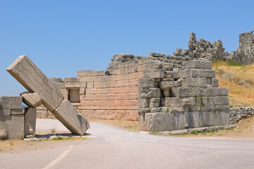 Fototapeta premium Ancient Messene city walls, historical Greek ruins collapsing. Ancient stone walls and a massive fallen block portray the historical ruins of Messene, Greece