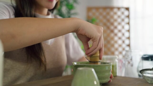 Close up of woman preparing matcha by stirring green tea powder in bowl.