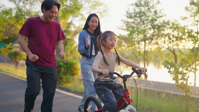 Asian young girl riding bicycle in garden while her parents look after. 