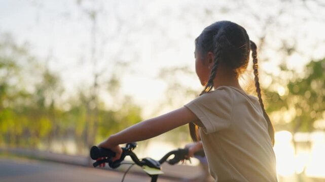 Asian young girl practicing riding a bicycle in a garden during sunset. 
