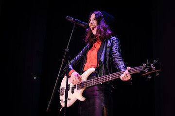 Fototapeta premium Punk rock girl with a grunge edgy style performing with a bass guitar. Female rock star with bold attitude and fierce stage presence creating an iconic live performance on black background.