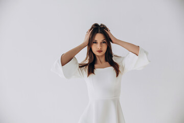Fototapeta premium Beauty portrait of a model, a beautiful brunette girl with straight long hair in a white dress, healthy and natural on a white background