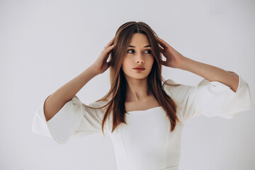 Naklejka premium Beauty portrait of a model, a beautiful brunette girl with straight long hair in a white dress, healthy and natural on a white background