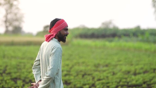 happy young indian farmer standing at green groundnut or  peanut agriculture farm	