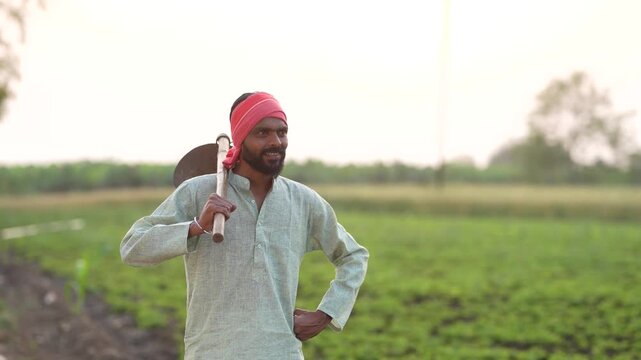 young indian farmer holding farming tool standing at field	