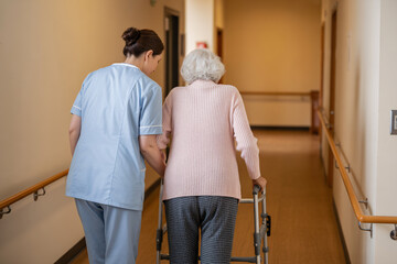 Fototapeta premium Female nurse helping older woman walk with walker in rehabilitation center hallway. Elder care and nursing support