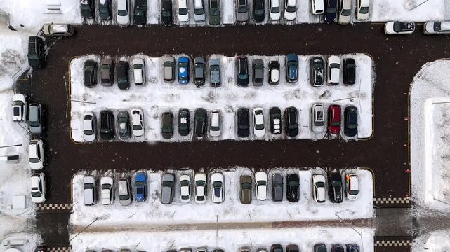 Snowy car park aerial view from a drone. It's snowing, cars are parked in the snow. High quality 4k footage