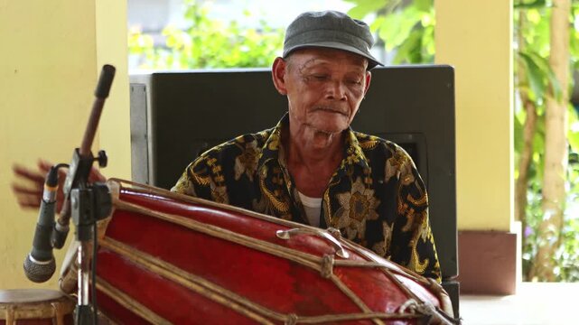 Elderly Indonesian musician playing a traditional kendang drum