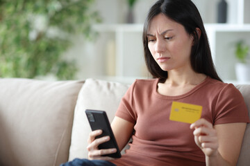 Annoyed asian woman paying online with credit card and phone