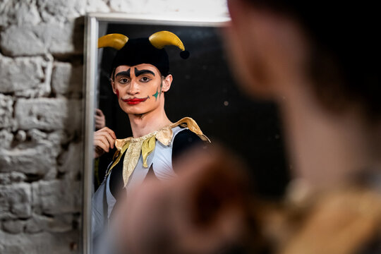 Man in jester costume  looking at his reflection in a mirror.