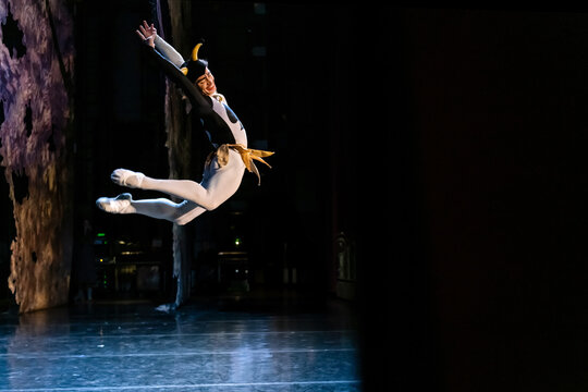 Man ballet dancer in a costume with horns jumping mid-air on stage.