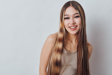 Naklejka premium Portrait of young woman smiling with long straight hair wearing casual sleeveless top on neutral background. Female model looking happy and relaxed with natural makeup and friendly expression.