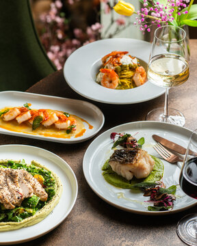 An exquisite restaurant table featuring spaghetti with king prawns, pan-seared white fish on pea puree, grilled scallops, and fresh tomato burrata bruschetta.