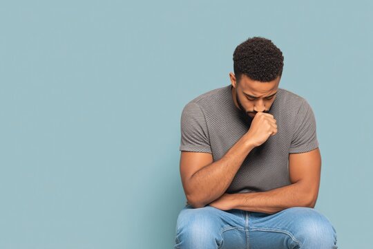 Coughing man seated with elbows on knees indoor setting emotional portrait thoughtful mood
