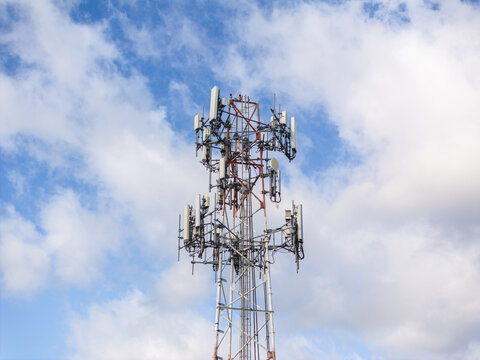 Aerial view of a cell phone tower piercing the vibrant blue sky dotted with fluffy white clouds, a stark contrast of technology and nature, Hollywood, Florida, United States.