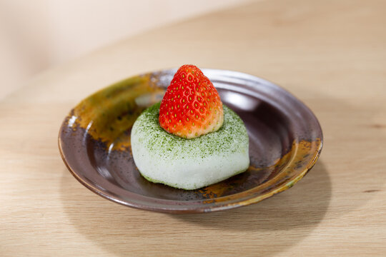 Soft and chewy matcha mochi topped with a fresh strawberry, served on a rustic ceramic plate. A minimal Japanese dessert highlighting natural colors and delicate texture.
