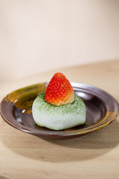 Soft and chewy matcha mochi topped with a fresh strawberry, served on a rustic ceramic plate. A minimal Japanese dessert highlighting natural colors and delicate texture.