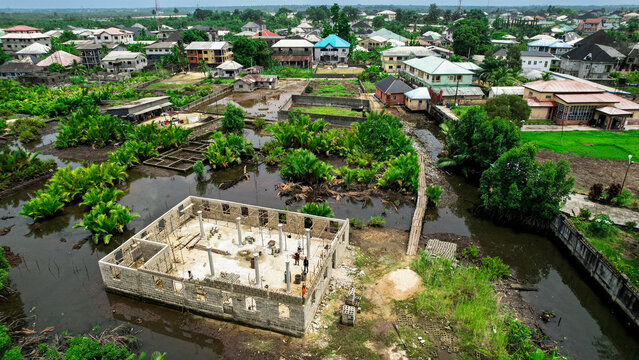 Aerial view of standing waters surround buildings under construction and established homes reflecting the sky in a watery mirror, Abonnema, Rivers, Nigeria.