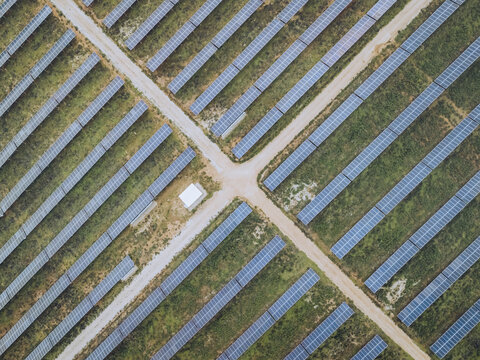 Aerial view of neatly arranged solar panels stretch across the landscape, intersected by pathways, creating a geometric pattern of blue and earthy tones, Lagos, Faro District, Portugal.