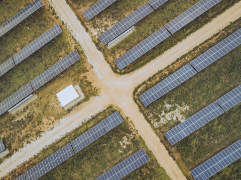 Aerial view of solar panels aligned in neat rows, reflecting the bright sunlight, bisected by sandy paths, creating a geometric pattern, Lagos, Faro District, Portugal.