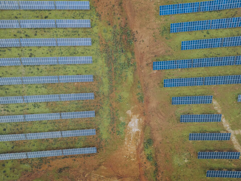 Aerial view of solar panels standing in rows against the contrast of earth tones and green vegetation, Lagos, Faro District, Portugal.