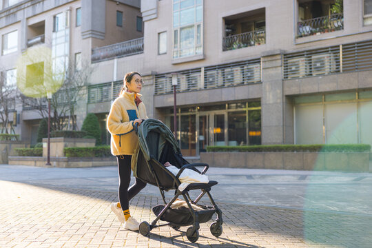 Mother pushing baby stroller outdoors in sunny park