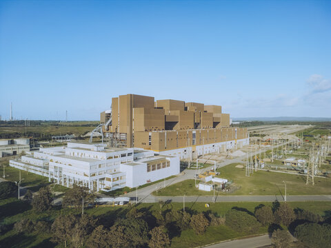 Aerial view of a large industrial hydrogen energy building complex with a mix of brown and white structures against a clear blue sky, Sines, Setubal, Portugal.