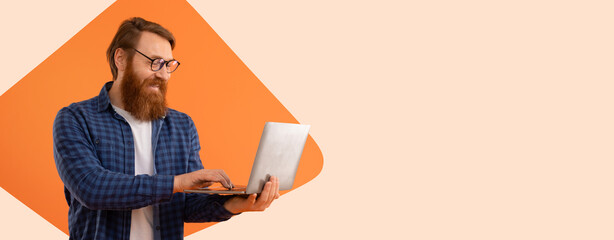 A man with a beard and glasses is using a laptop while standing. He seems focused on the screen....