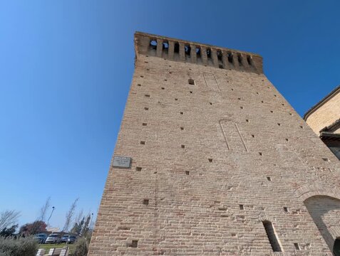 Torre medievale in pietra immersa in un contesto urbano contemporaneo, con cielo limpido, luce naturale e dettagli architettonici ben definiti