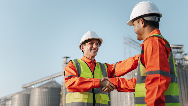 Two engineers wearing safety helmets shake hands, proposing a collaboration agreement for a project to construct a factory.