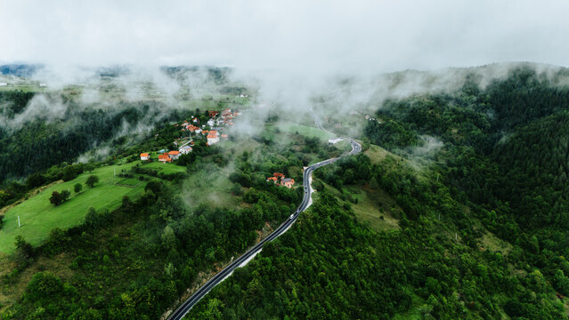Aerial view of winding roads cutting through verdant hills, nestled villages with terracotta roofs shrouded in ethereal mist, Romanija, Republika Srpska, Bosnia and Herzegovina.
