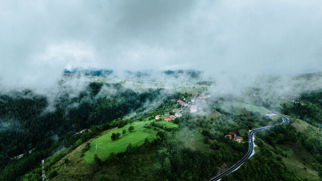 Aerial view of houses nestled amidst the lush green hills, partially obscured by a blanket of ethereal fog, Romanija, Republika Srpska, Bosnia and Herzegovina.