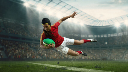 Naklejka premium Female rugby player diving with ball in mid air on stadium field. Concept of fearless performance, extreme effort, professional women competition and high energy sports promotion.