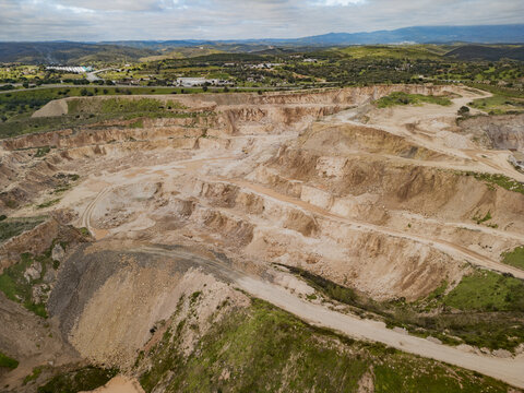Aerial view of a sprawling quarry revealing layers of earth, contrasting sharply with the verdant hills in the background, Alvor, Faro District, Portugal.