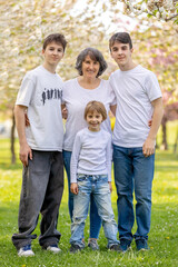 Fototapeta premium Portrait of cute stylish smiling family, boys and grandmother sitting in the grass in park