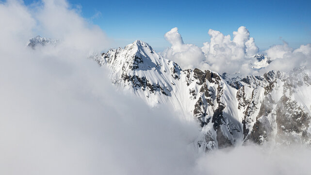 Aerial view of majestic, snow-capped mountain peaks piercing through a sea of ethereal clouds under a bright azure sky, Arigna, Orobie Alps Natural park, Lombardy, Italy.