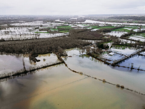Isle-Saint-Georges, France - 20 February 2026: Aerial view of a mosaic of flooded fields reflecting the somber sky, punctuated by the dark silhouettes of trees and the faint green of submerged crops.