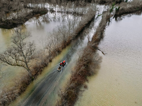 Isle-Saint-Georges, France - 20 February 2026: Aerial view of a red tractor braving the floodwaters on a submerged road, flanked by bare trees and murky waters, a stark reminder of nature's power.