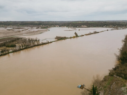 Aerial view of the muddy Garonne River overflowing its banks, swallowing the agricultural fields under a dull, overcast sky, Portets, Nouvelle-Aquitaine, France.