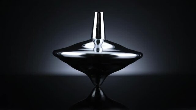 A sleek, dark metallic spinning top toy in perfect balance, creating a mesmerizing visual effect with its reflection on a glossy surface. Ideal for concepts of stability, precision, and focus.